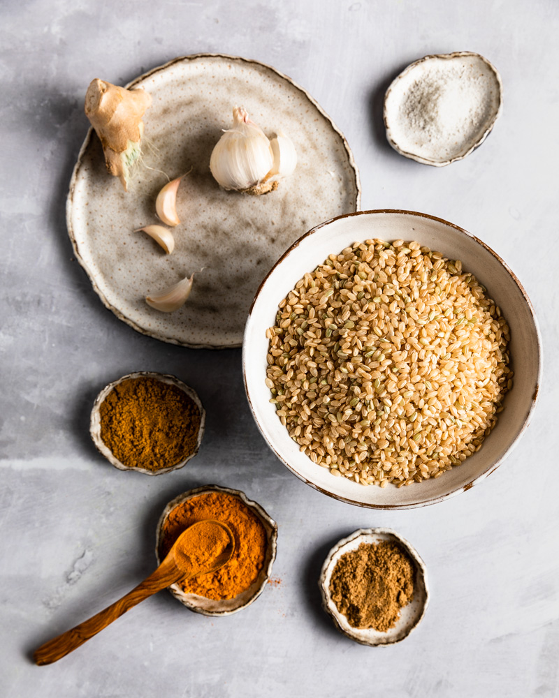 An arrangement of ingredients for Fragrant Golden Rice: short grain rice, garlic, ginger, coriander, cumin, turmeric, and salt