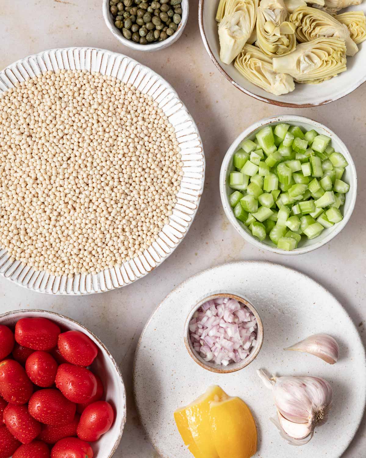 An overhead view of the ingredients needed for this recipe, including pearl couscous, tomatoes, celery, and artichoke hearts